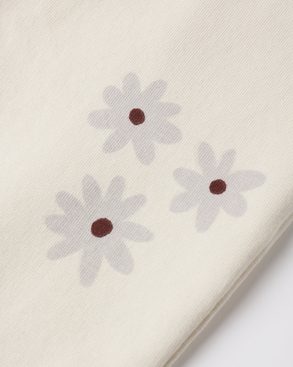 Close-up of a cream-colored fabric with three light gray daisy flowers printed on it, each with a small dark brown center.