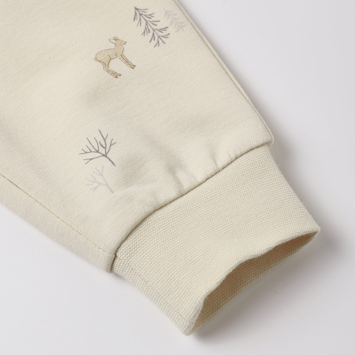 Close-up of a cream-colored sweatshirt sleeve featuring a small embroidered deer and delicate tree motifs near the ribbed cuff.