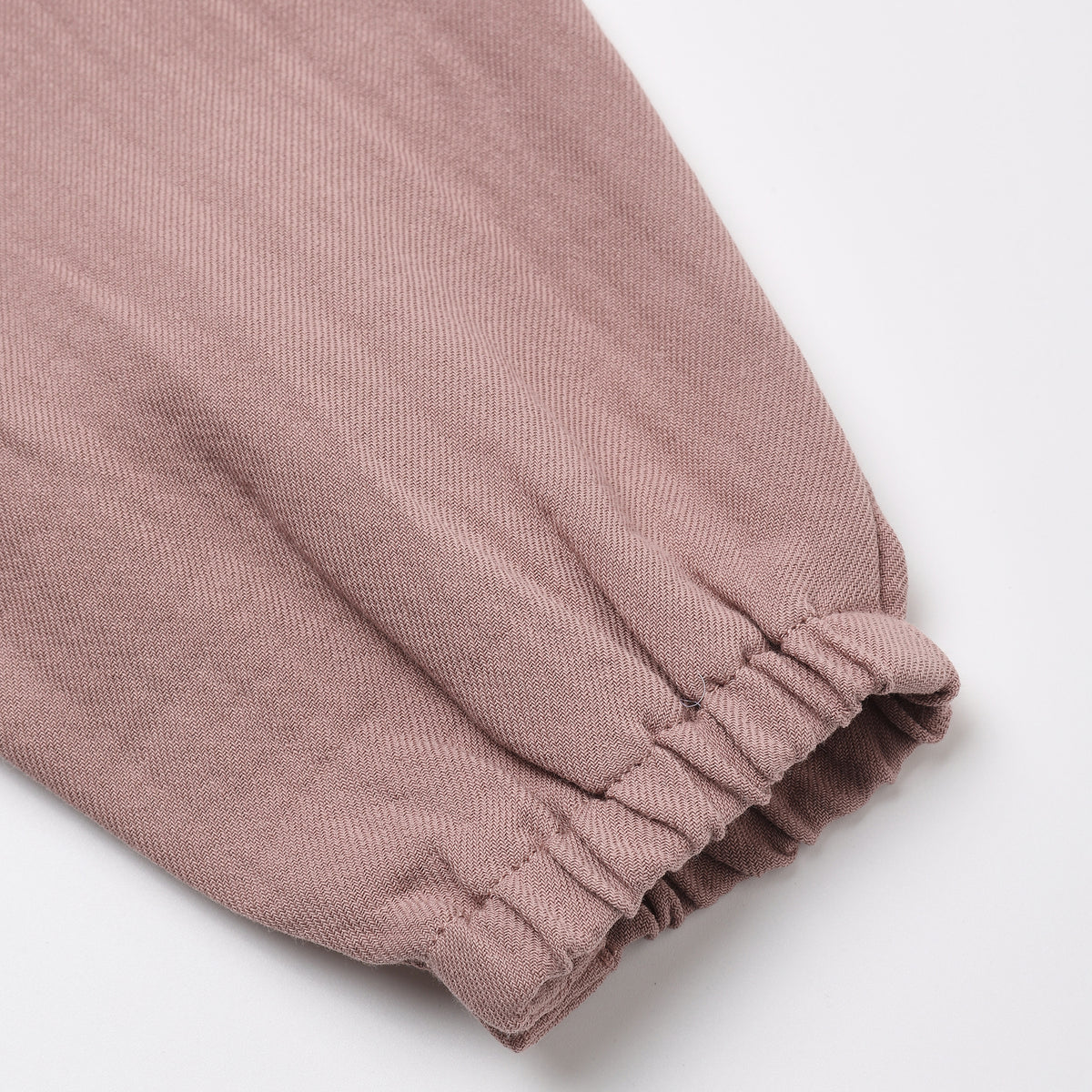 A close-up of a dusty rose or mauve-colored fabric garment, showing a gathered elastic cuff on a plain white background.
