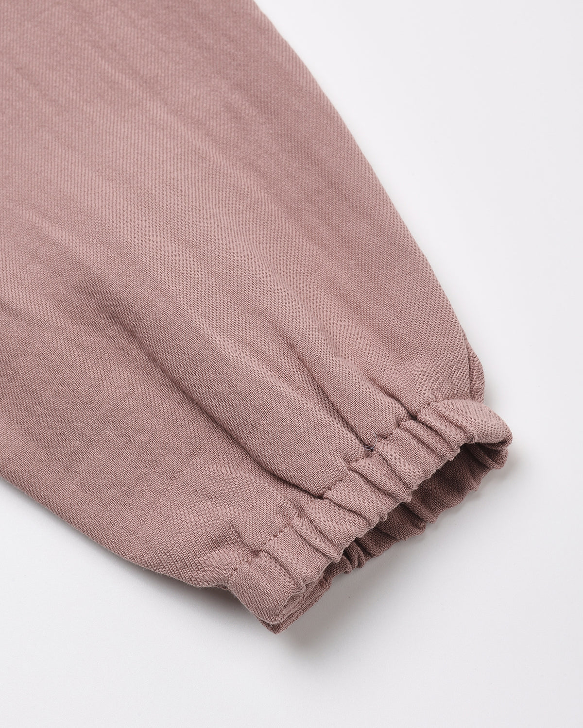 A close-up of a dusty rose or mauve-colored fabric garment, showing a gathered elastic cuff on a plain white background.