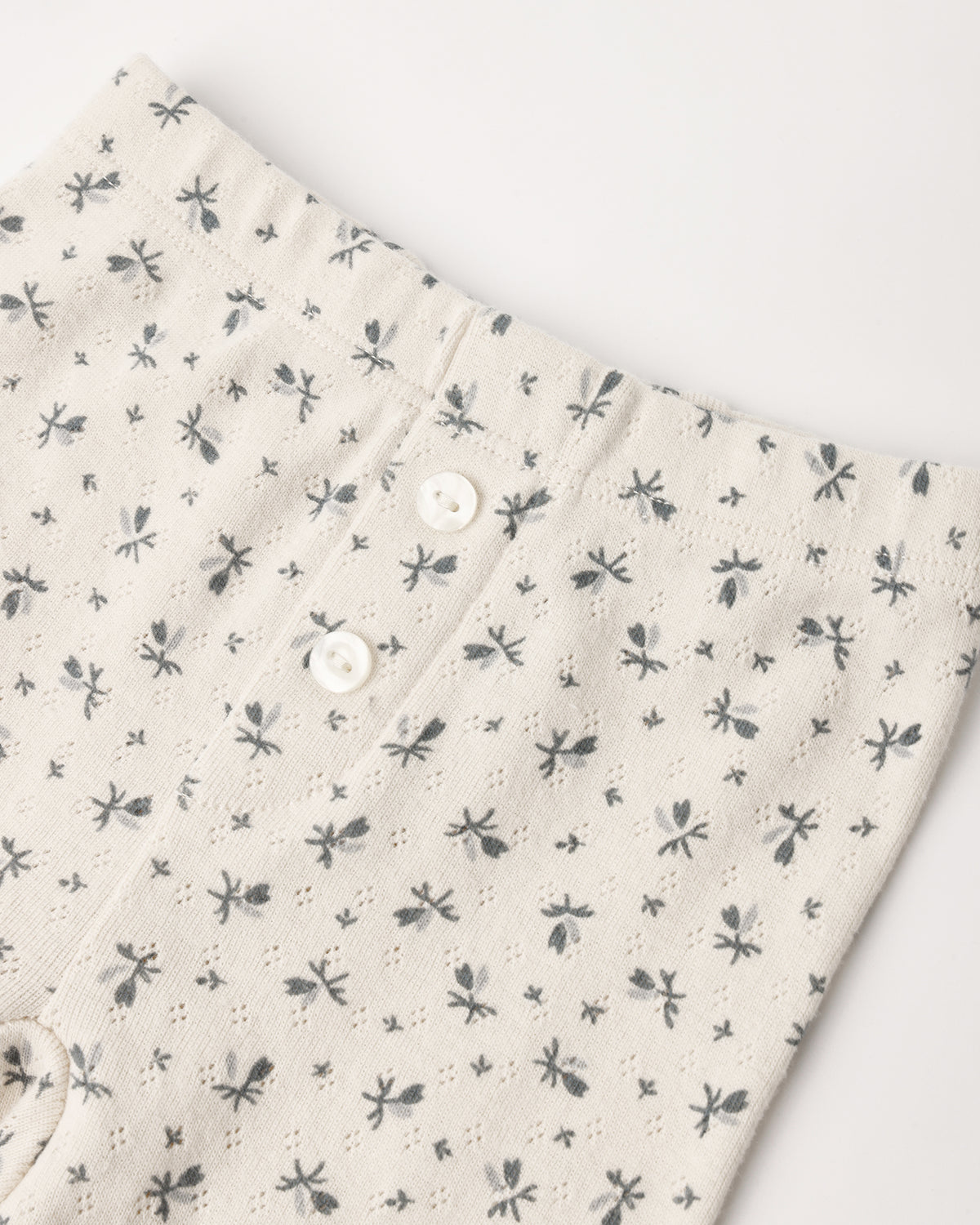 A pair of cream-colored pointelle cotton baby leggings featuring a delicate ditsy floral print and decorative front buttons
