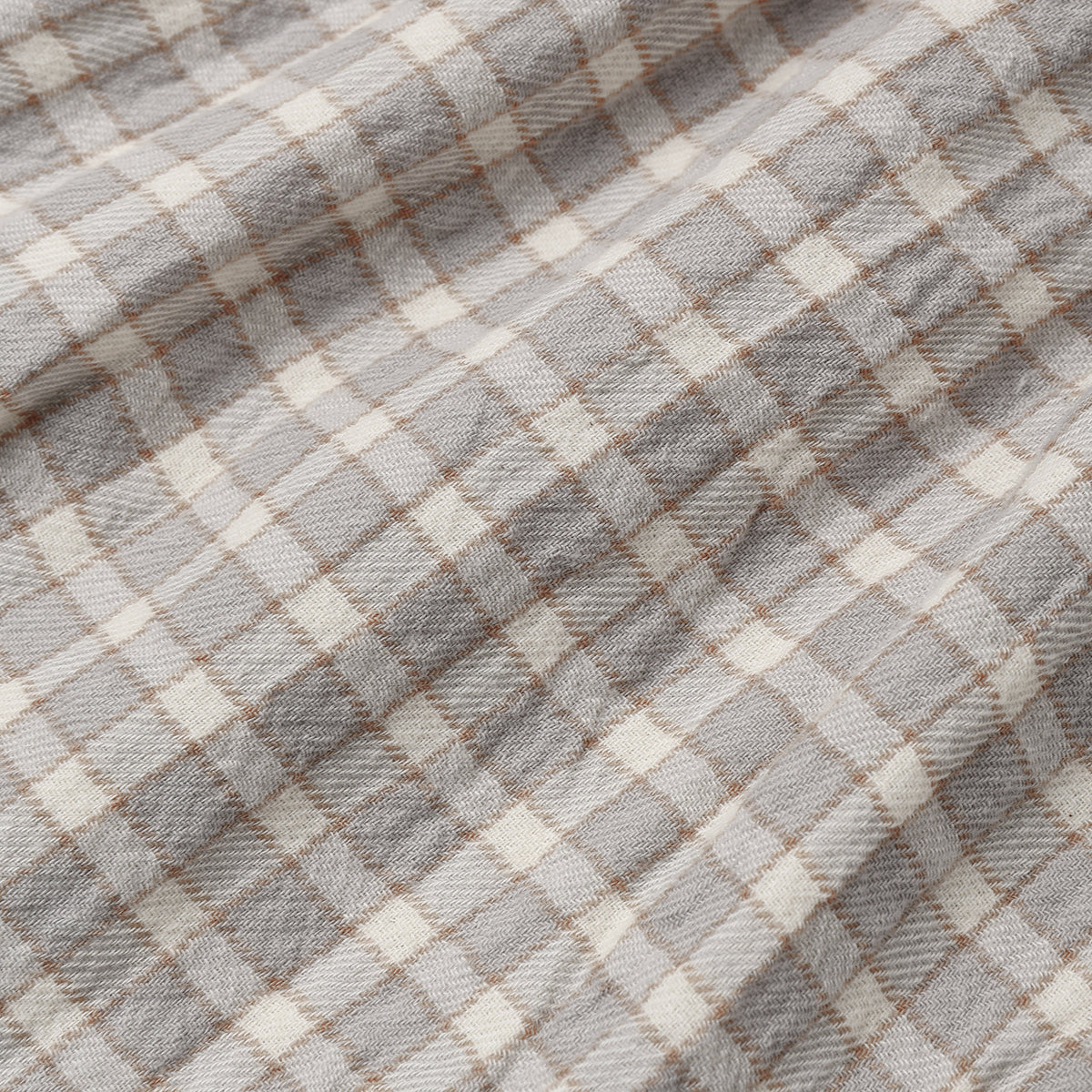 A close-up of a plaid fabric with a gray and off-white checkered pattern and thin brown intersecting lines.