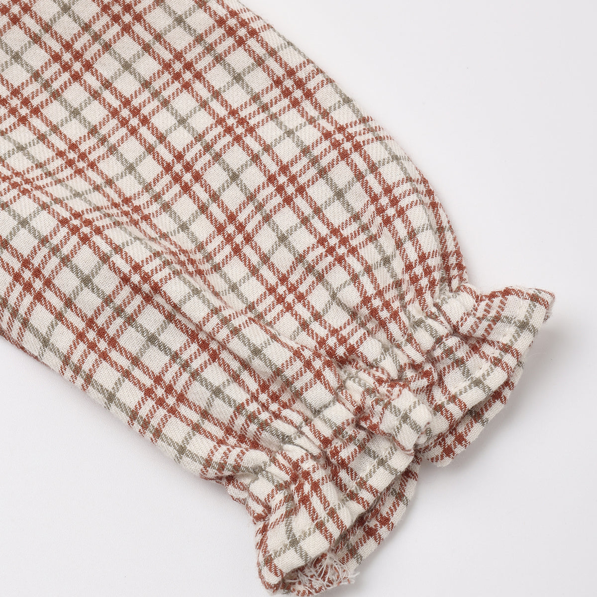 Close-up of a long-sleeve baby dress in a red, white, and tan Christmas plaid pattern, featuring a smocked cuff with a ruffled trim.
