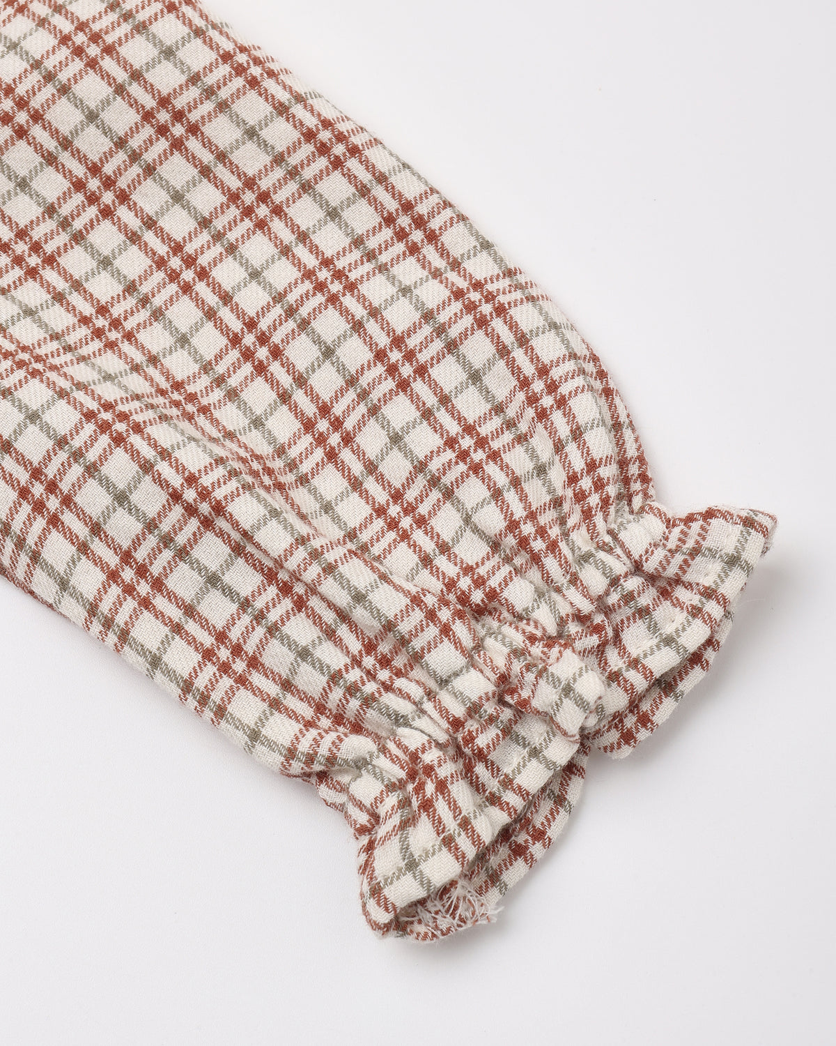 Close-up of a long-sleeve baby dress in a red, white, and tan Christmas plaid pattern, featuring a smocked cuff with a ruffled trim.