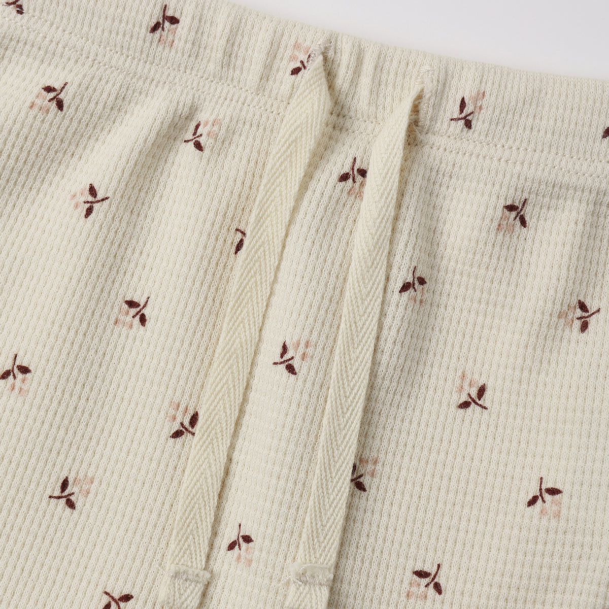 Close-up of a cream-colored waffle-knit fabric with a small brown and dusty pink floral print, featuring a matching cream drawstring waist.