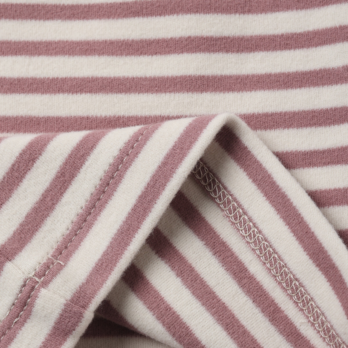 Close-up of a striped fabric with alternating dusty rose and off-white horizontal stripes, showing a folded corner with stitched edges.