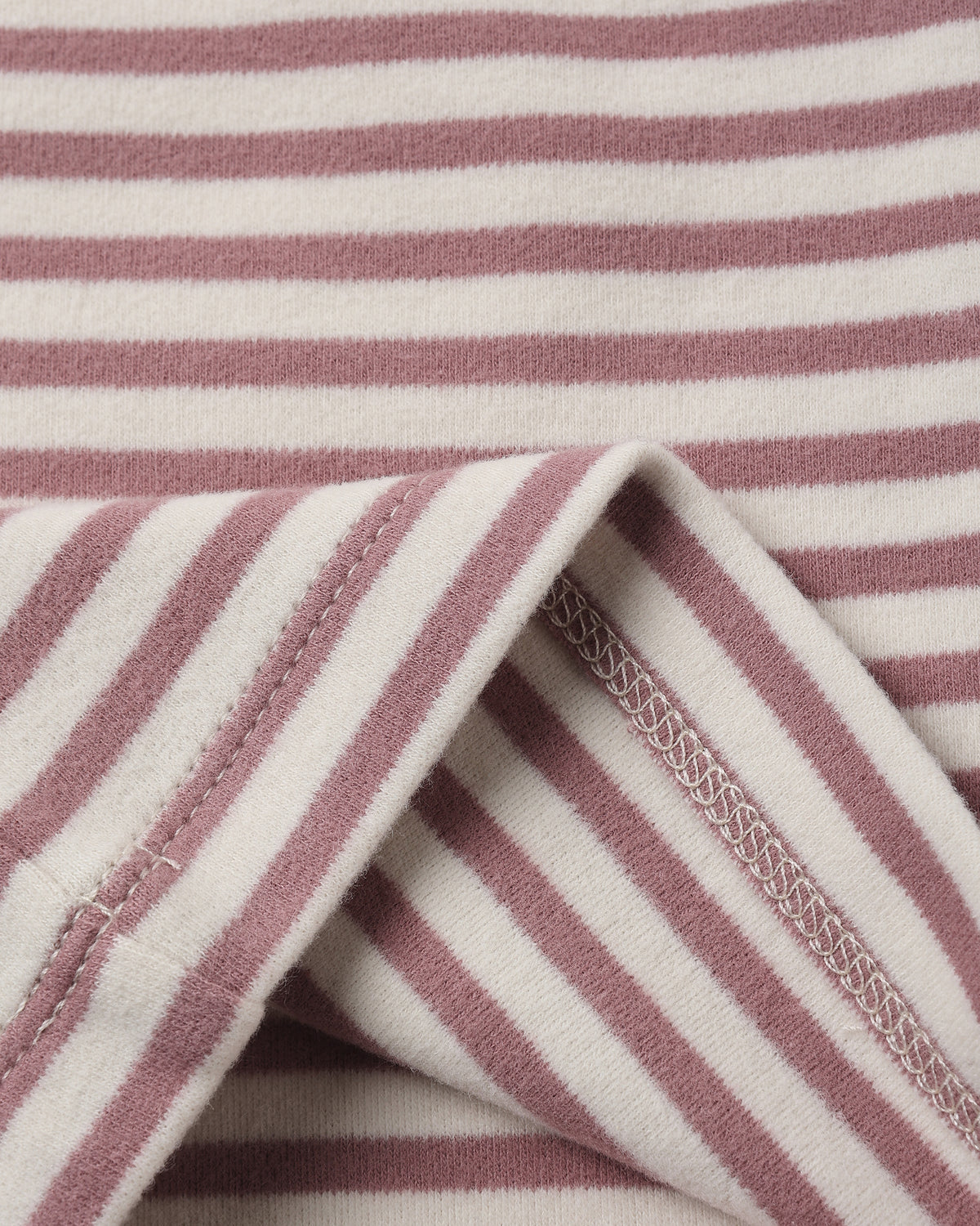 Close-up of a striped fabric with alternating dusty rose and off-white horizontal stripes, showing a folded corner with stitched edges.