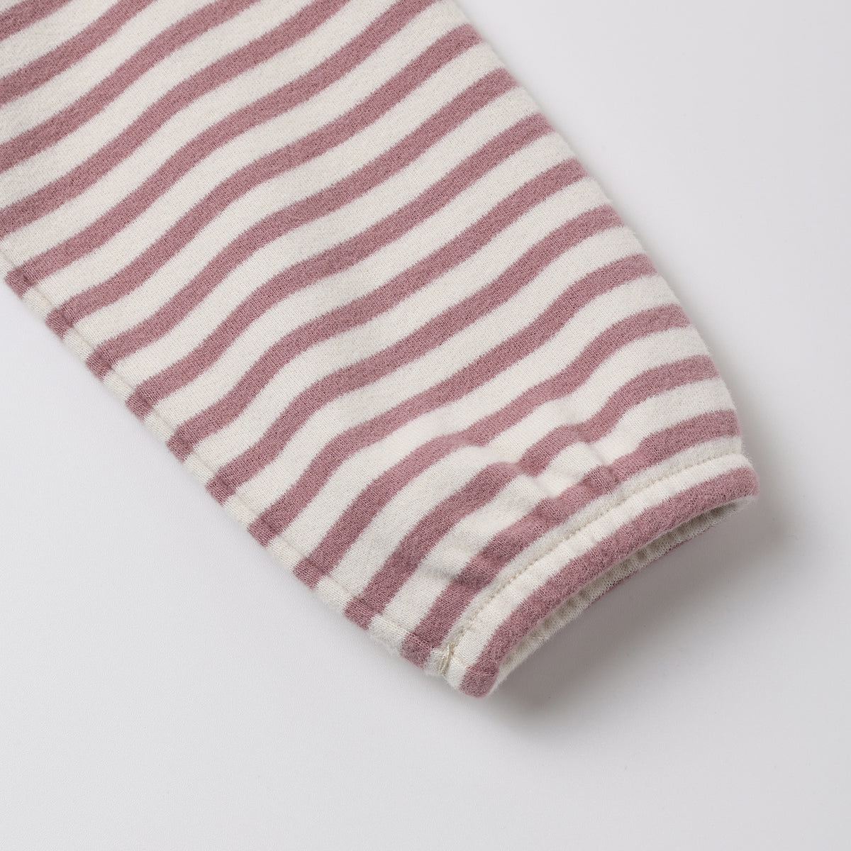 A close-up of a striped fabric sleeve or cuff with alternating dusty rose and off-white horizontal stripes, finished with a ribbed hem, on a light gray background.