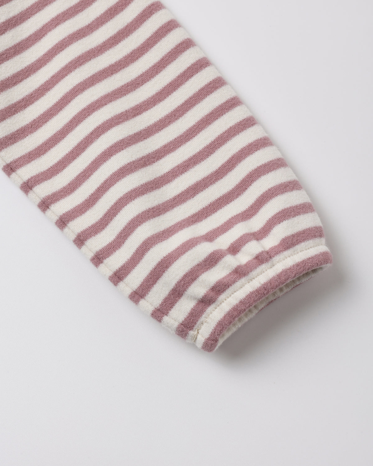 A close-up of a striped fabric sleeve or cuff with alternating dusty rose and off-white horizontal stripes, finished with a ribbed hem, on a light gray background.