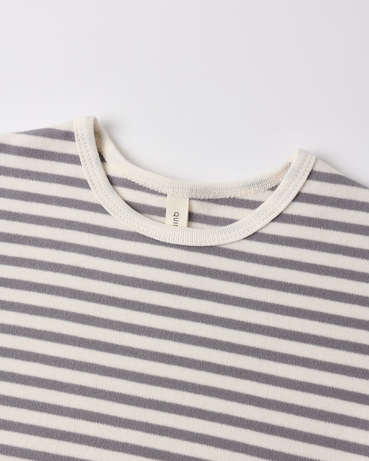Close-up of a striped knit top with alternating gray and off-white horizontal stripes, featuring a cream ribbed crew neck and a small interior neck label reading 'GANT'.
