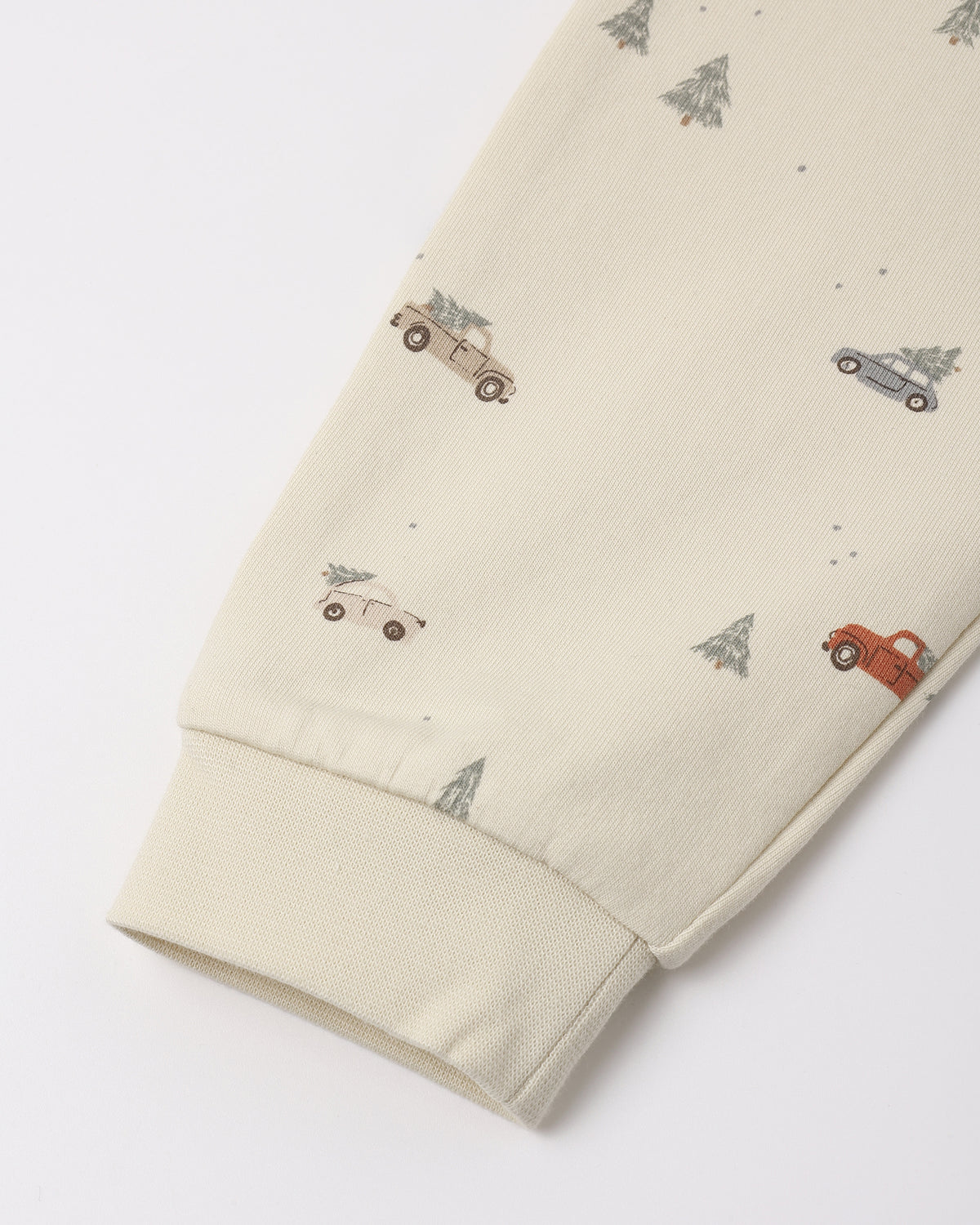 Close-up of cream-colored organic cotton fabric featuring a "Holiday Drive" print with tiny vintage cars and pine trees, showing a ribbed sleeve cuff.