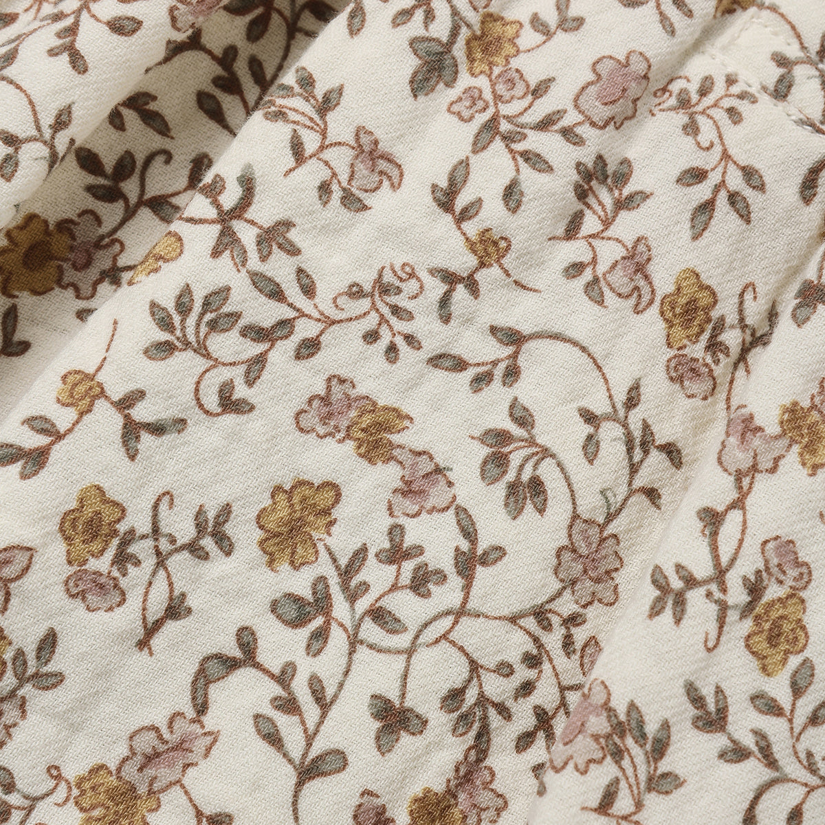 A close-up of a cream-colored fabric with an intricate floral vine pattern in muted brown, dusty pink, and mustard yellow.