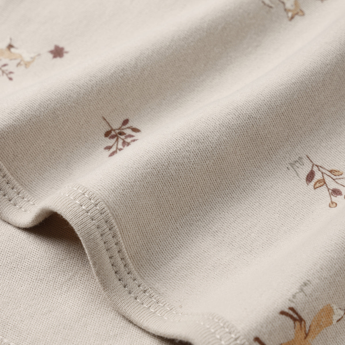 Close-up of a cream-colored knit fabric with a delicate print of small brown and tan woodland animals and leaves, showing the fine knit texture and neat stitching.
