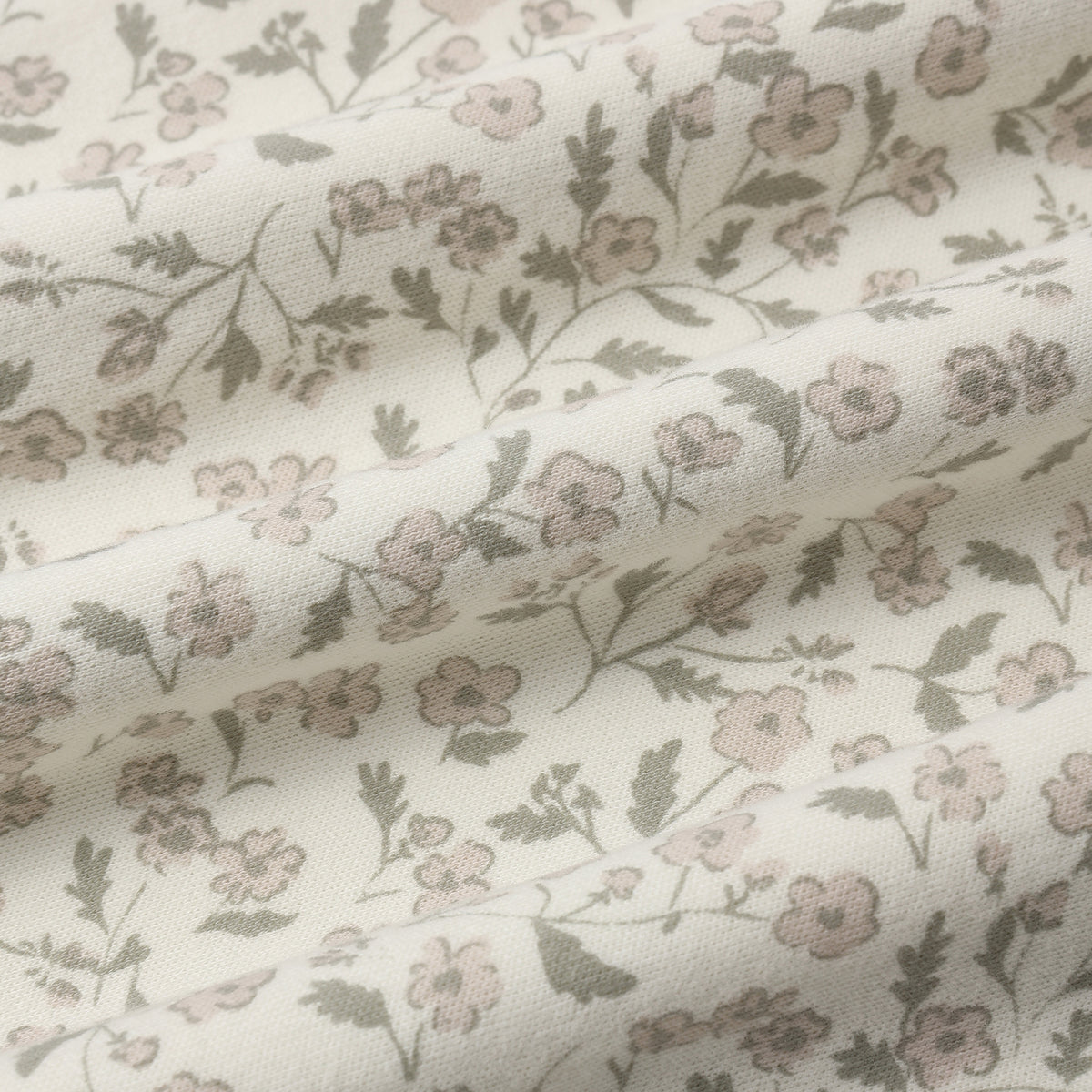 A close-up of a draped fabric with a delicate floral pattern in muted pink and olive green on an off-white background.