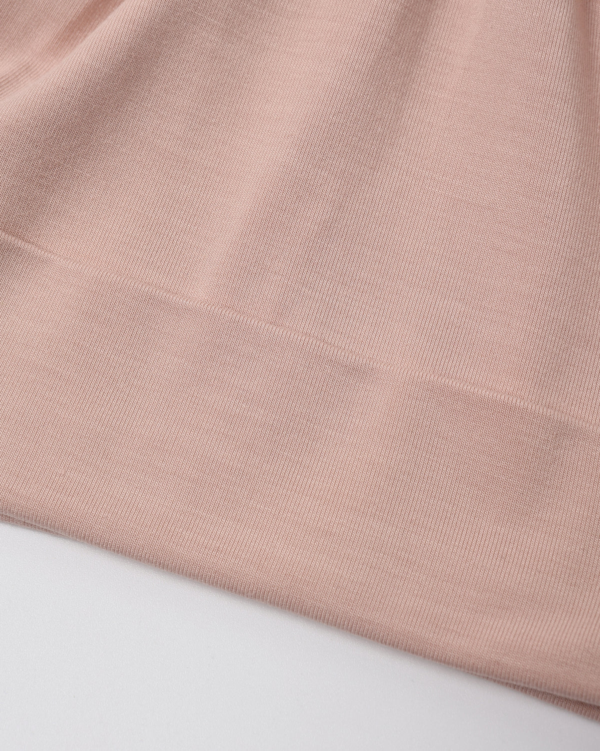 A close-up of a dusty pink ribbed knit fabric, showing the fine texture and folded hem, set against a plain white background.