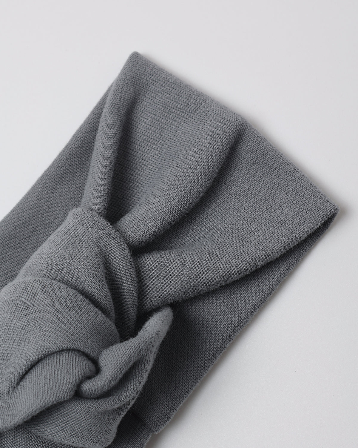 A folded dark gray knit headband with a twisted knot detail, shown on a light gray background.
