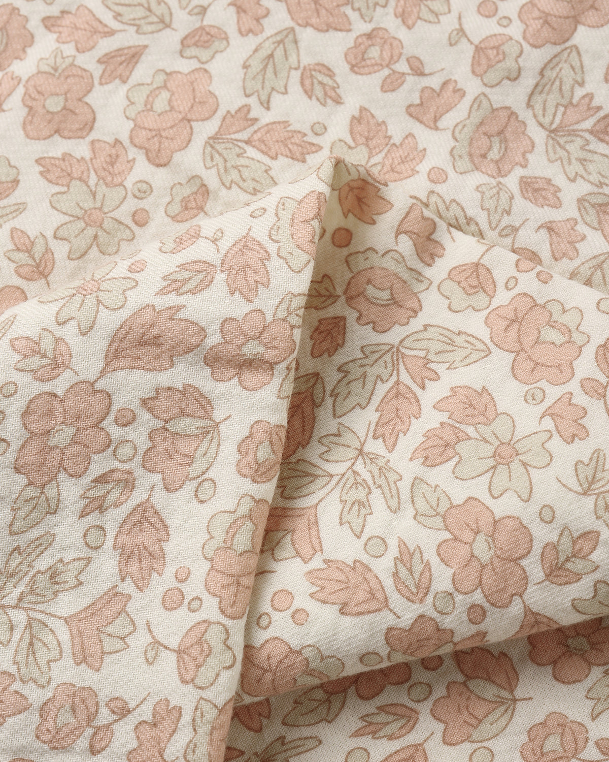 A close-up of a cream-colored fabric with a delicate floral pattern in dusty pink and muted sage green, featuring soft folds.
