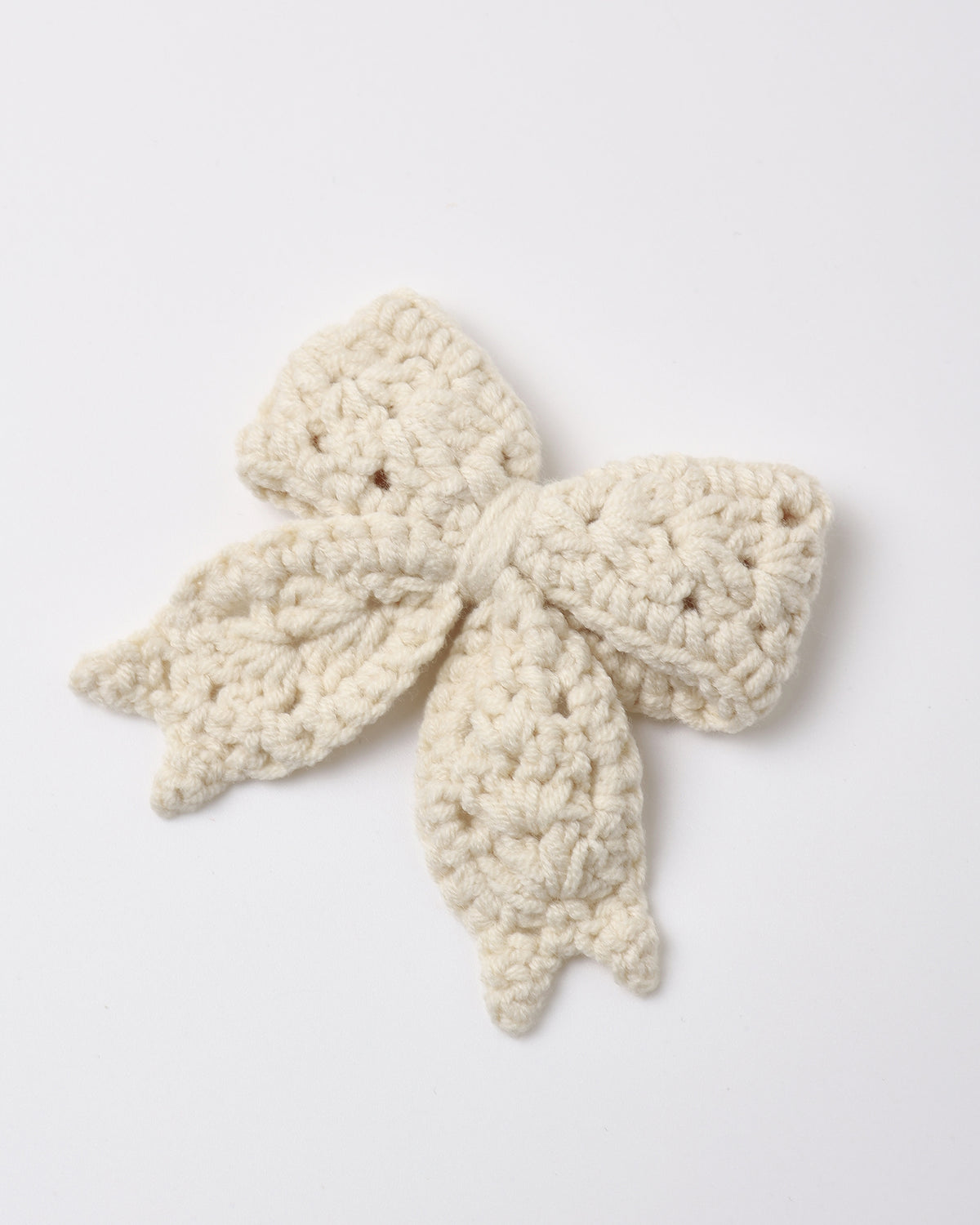 A natural-colored crochet hair bow made of 100% organic cotton, featuring a delicate textured design and attached to a gold alligator clip.