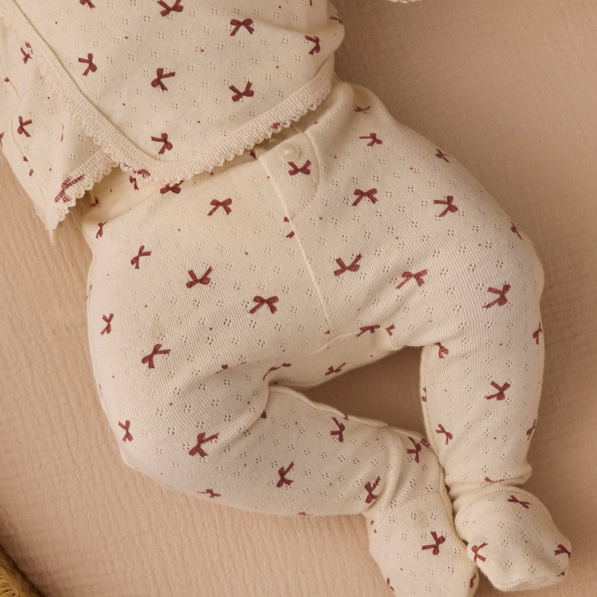 Close-up of an infant's legs and torso wearing the Quincy Mae red bows print long-sleeve top and footed pants.