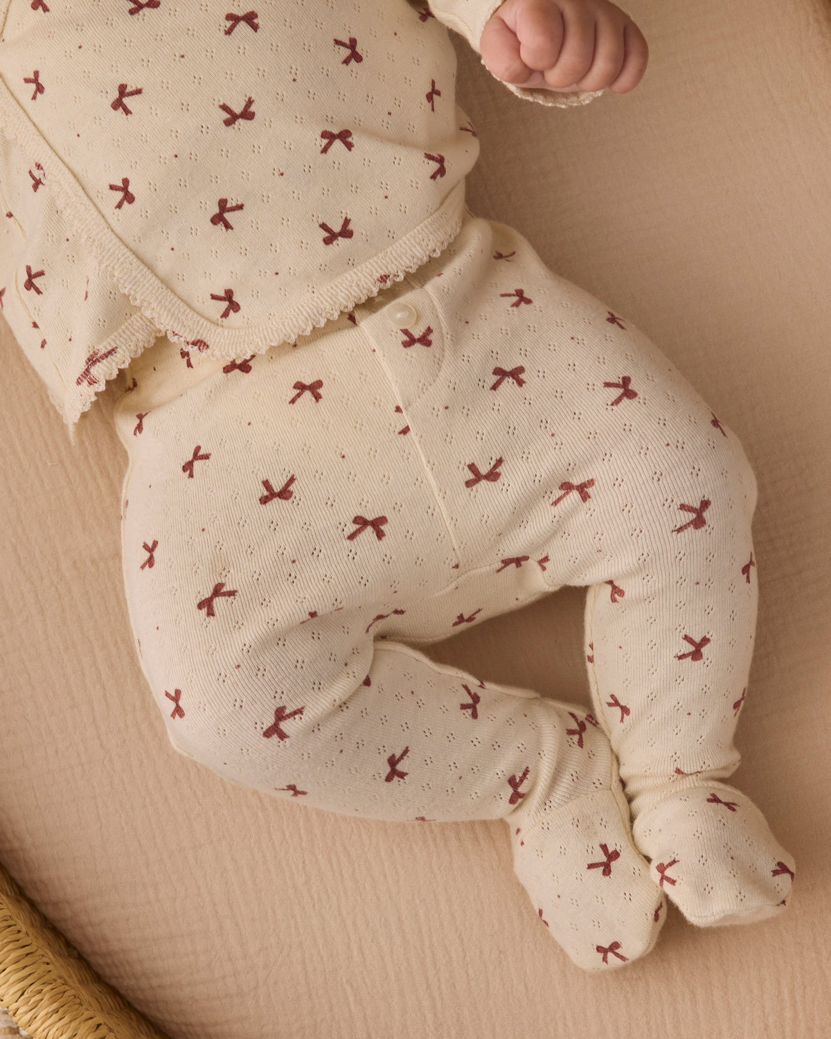 Close-up of an infant's legs and torso wearing the Quincy Mae red bows print long-sleeve top and footed pants.