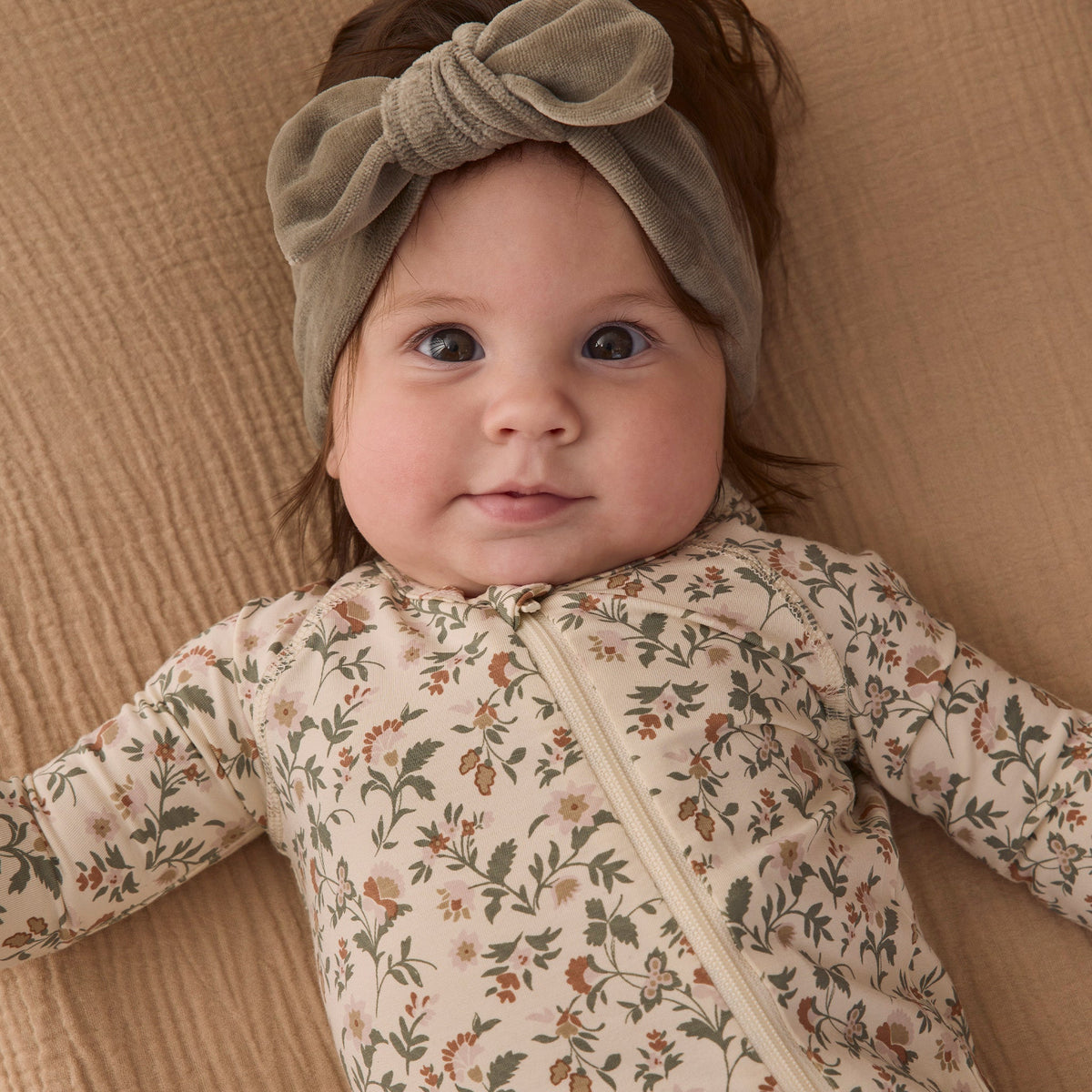 A baby wearing a sage green velour bow headband by Quincy Mae and a floral print organic cotton sleeper.