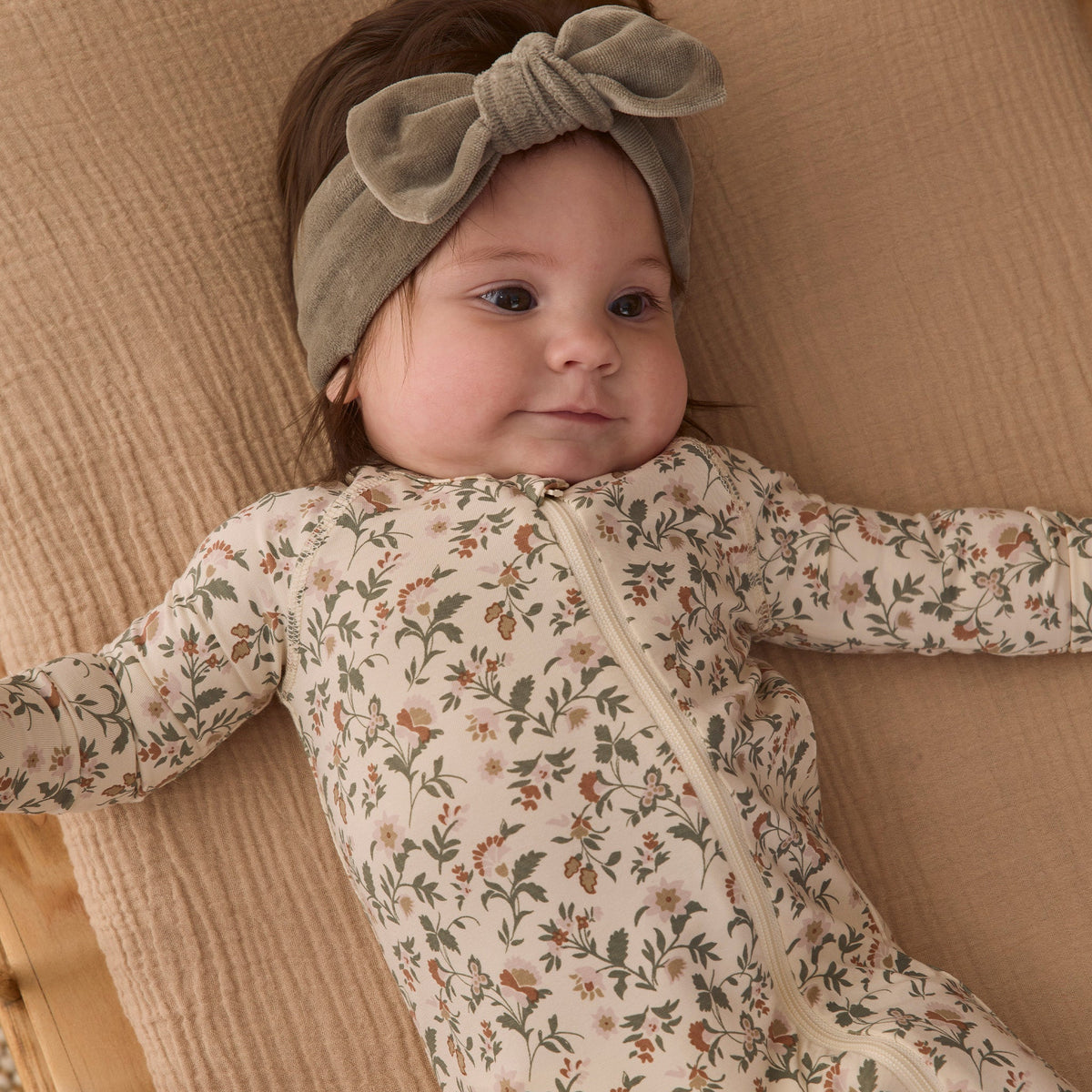 A baby wearing a sage green velour bow headband by Quincy Mae and a floral print organic cotton sleeper.