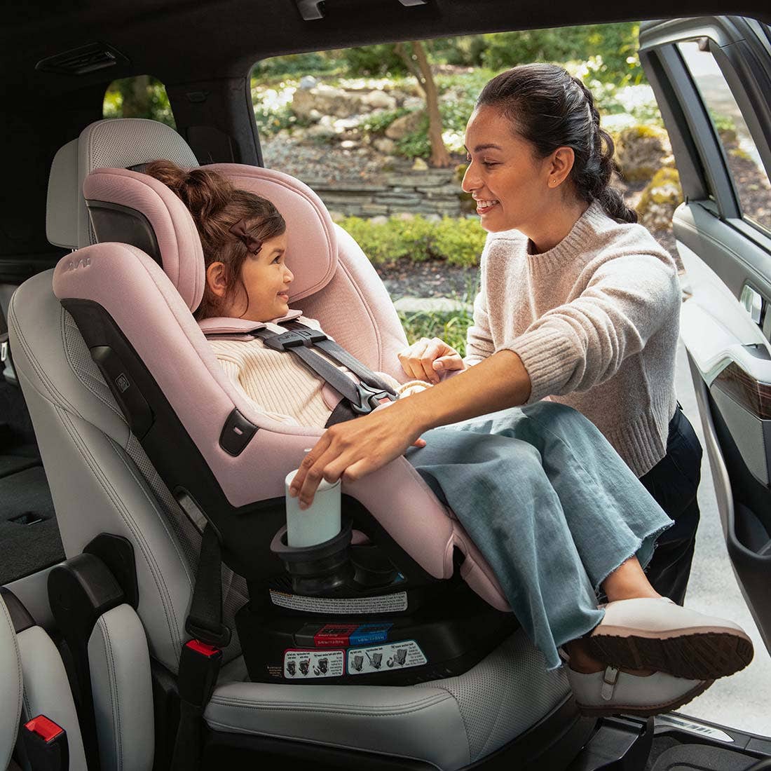 Woman adjusting a child in a pink car seat inside a vehicle.