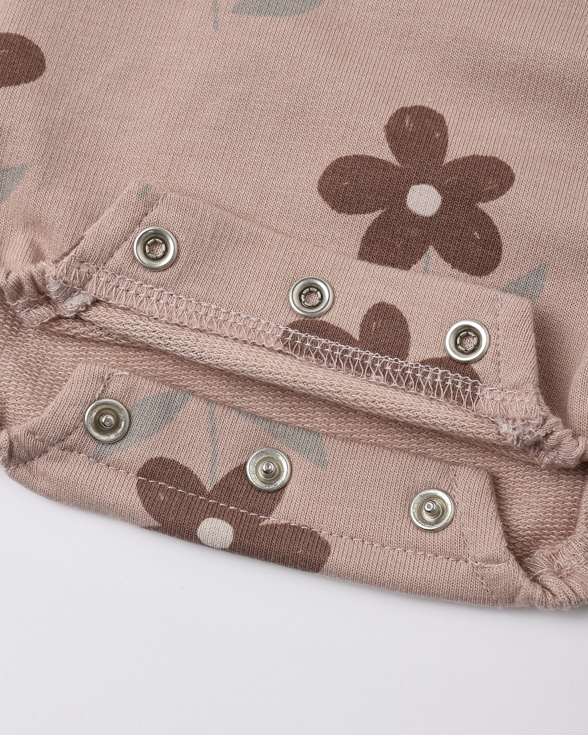 Close-up of a dusty pink fabric garment with a brown floral print and silver metal snap buttons.