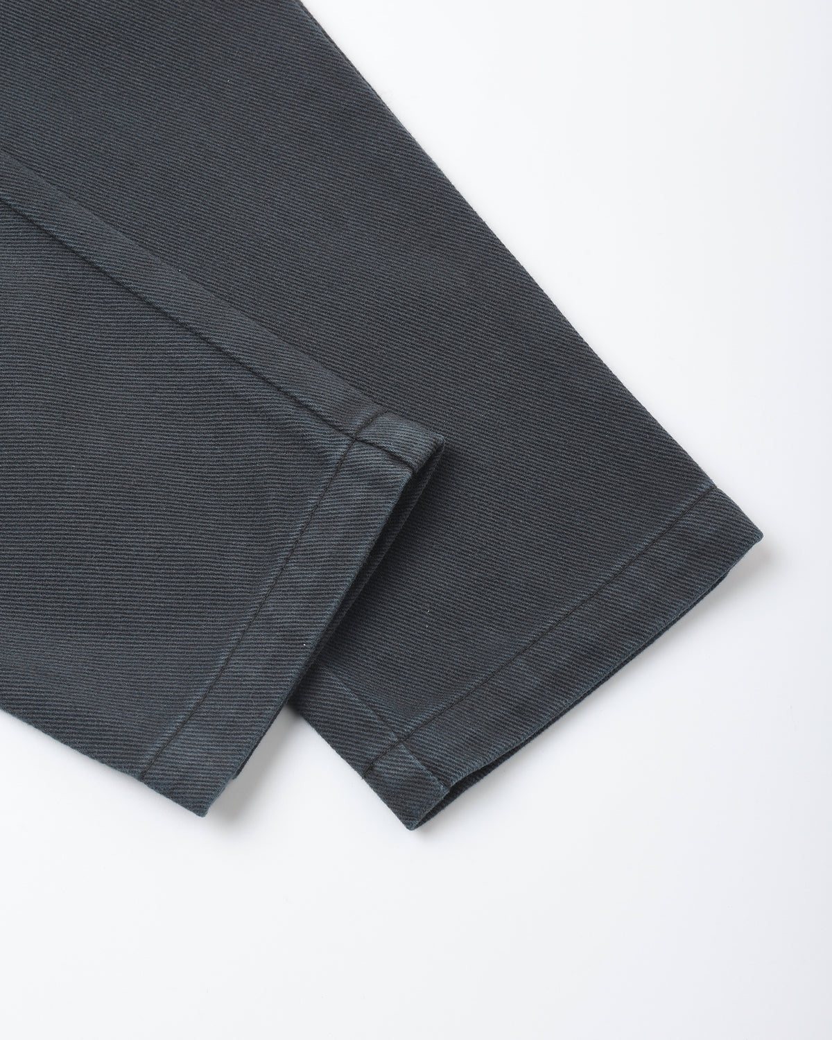 A close-up of folded dark charcoal gray fabric, showing the texture and hem detail against a clean white background.