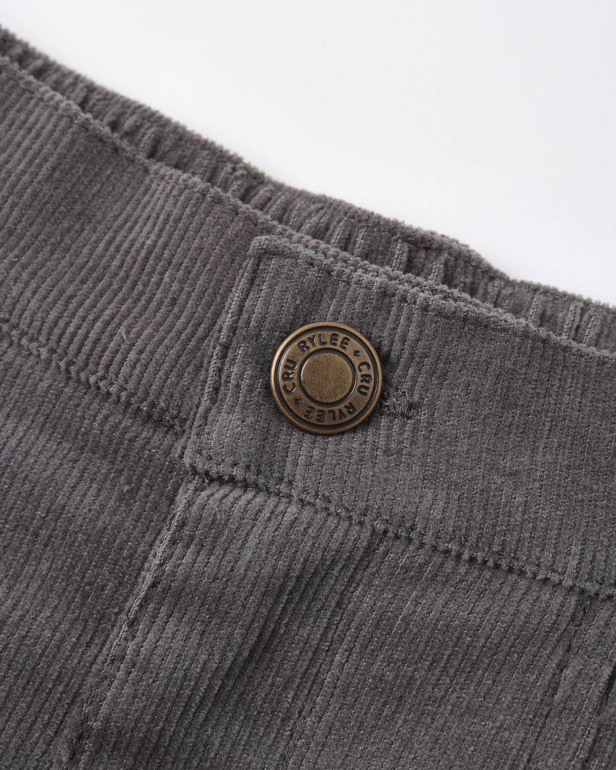 Close-up of dark gray corduroy trousers showing the waistband, button closure, and ribbed fabric texture against a white background.