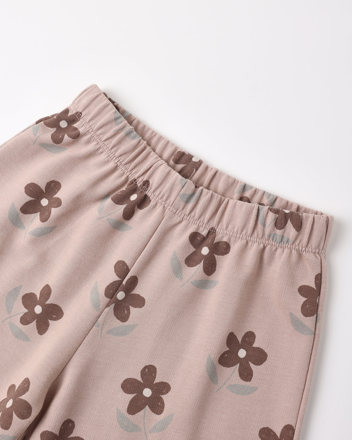 Close-up of a pair of light pink pants with an elastic waistband, featuring an all-over print of brown flowers with light blue-green leaves, shown on a plain white background.