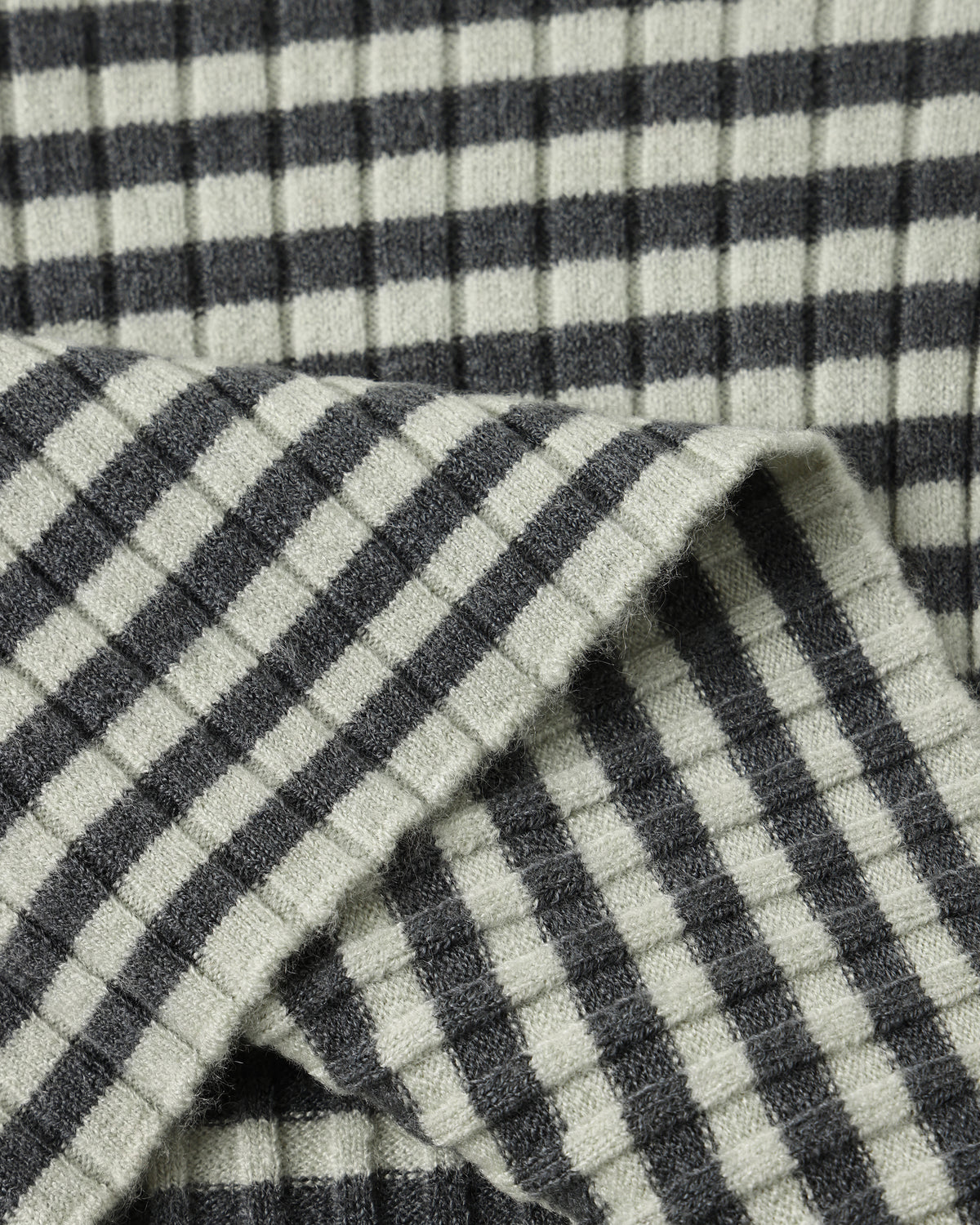 Close-up of a ribbed knit fabric with a dark gray and off-white gingham check pattern, folded to show texture and weave.