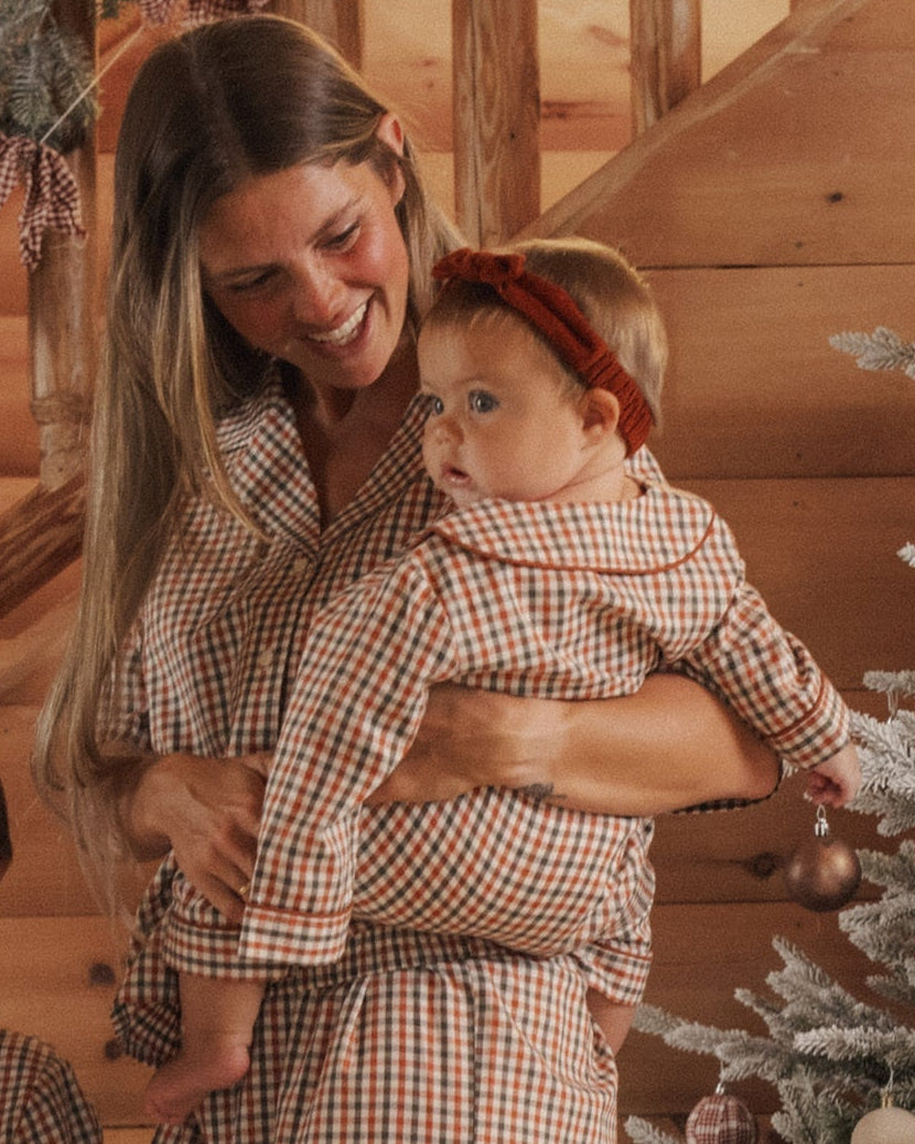A baby wearing plaid pajamas and a rust-brown corduroy headband with a knotted bow detail.