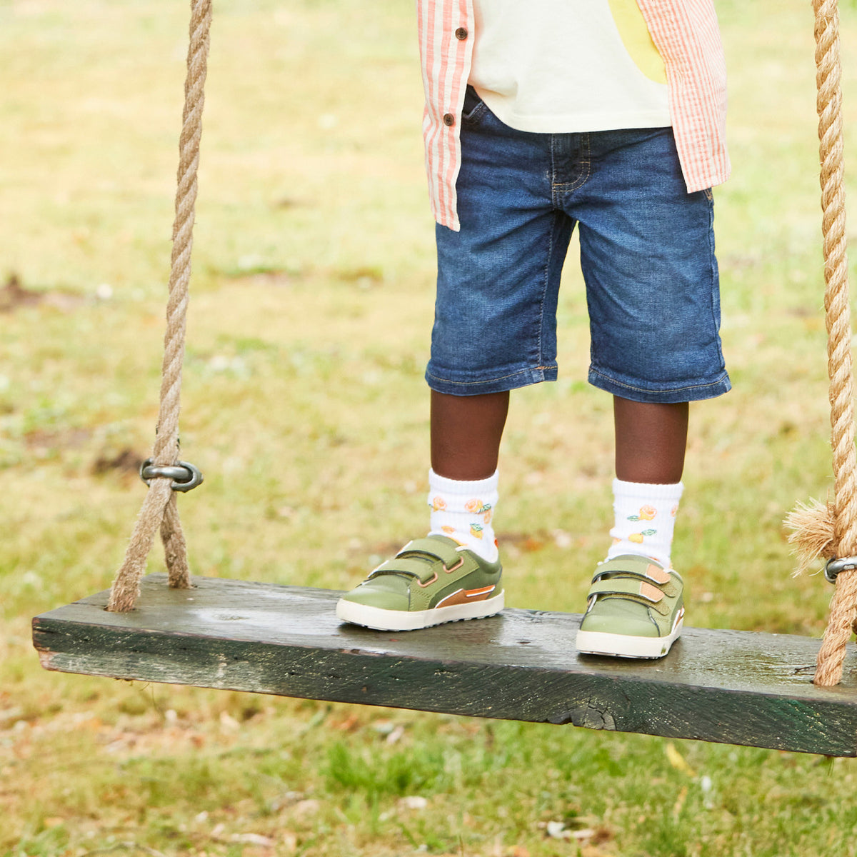 Child standing on a wooden swing with a grassy background