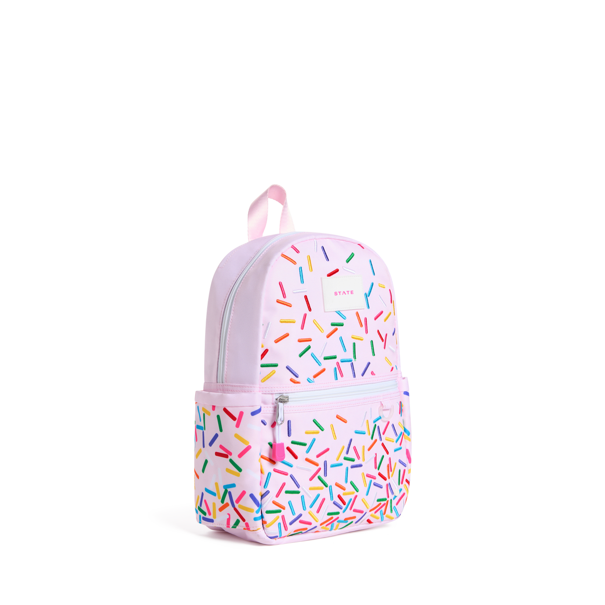 A light pink backpack with a colorful sprinkle pattern, featuring a top handle, main zippered compartment, and a front zippered pocket. The brand name 'KIKIKIK' is visible on the upper right side of the bag.