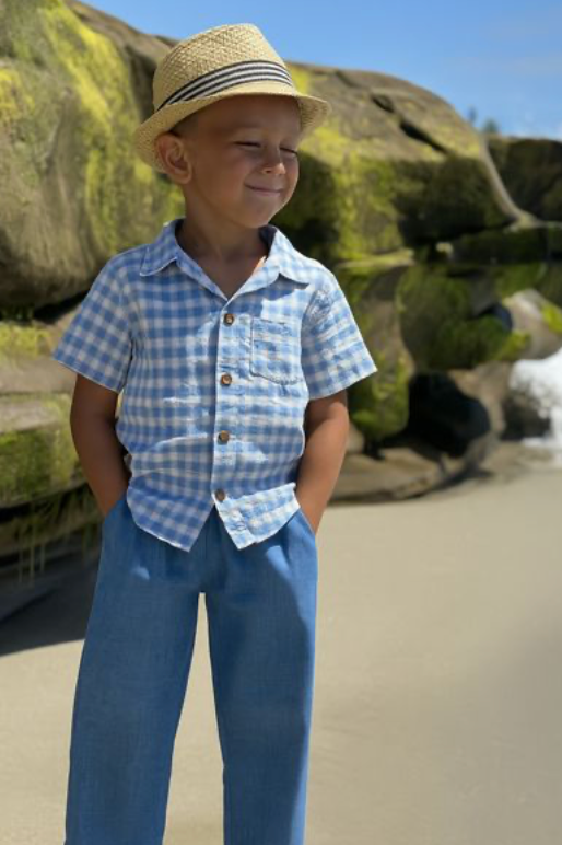 Child wearing a blue checkered shirt and straw hat standing in front of large rocks.