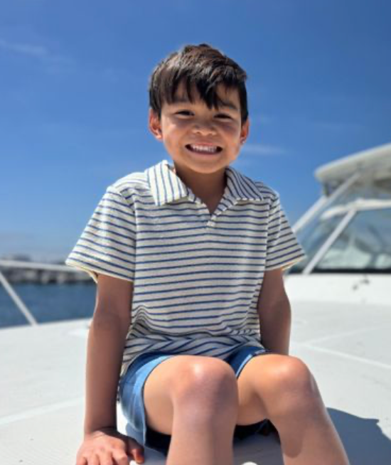 Child sitting on a boat deck with a clear blue sky background