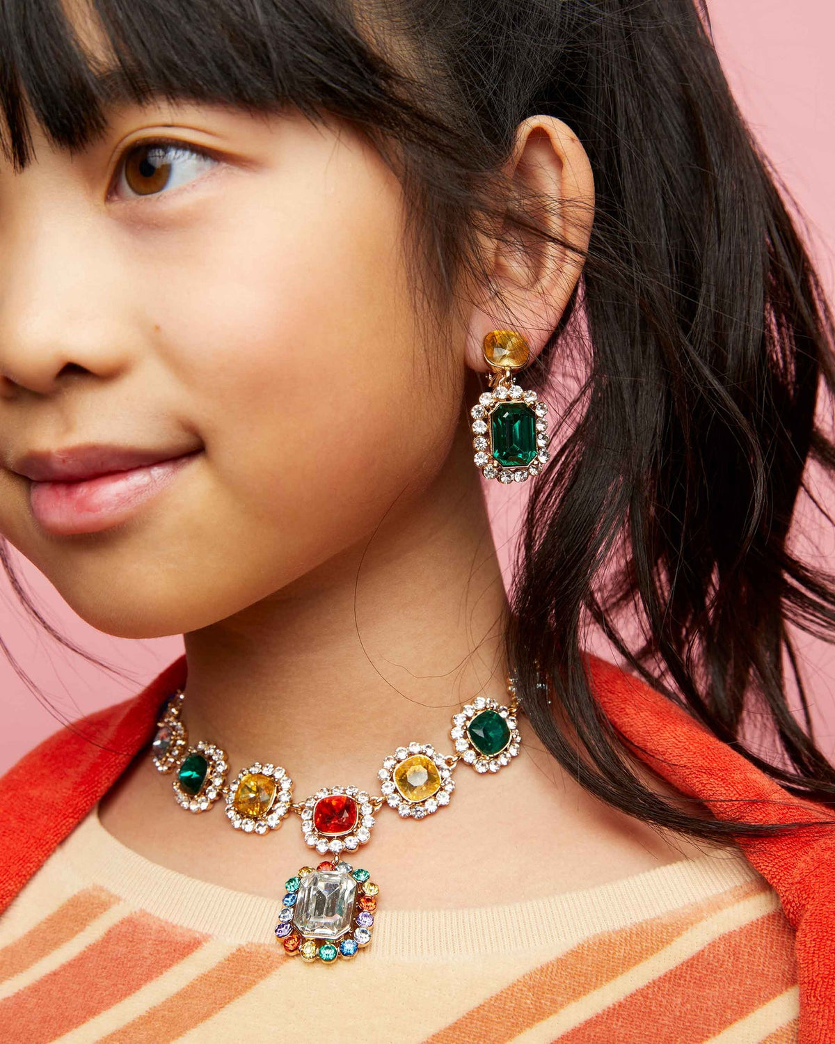 Close-up of a young girl wearing colorful gemstone jewelry against a pink background