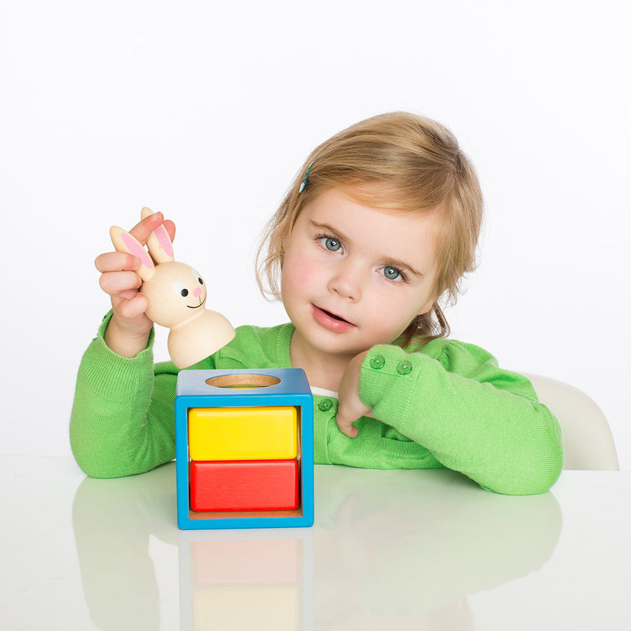 Child playing with a colorful toy block and wooden rabbit figurine on a white background