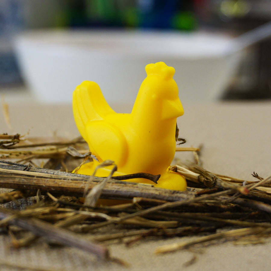 Yellow chicken-shaped object on a bed of straw with a blurred background