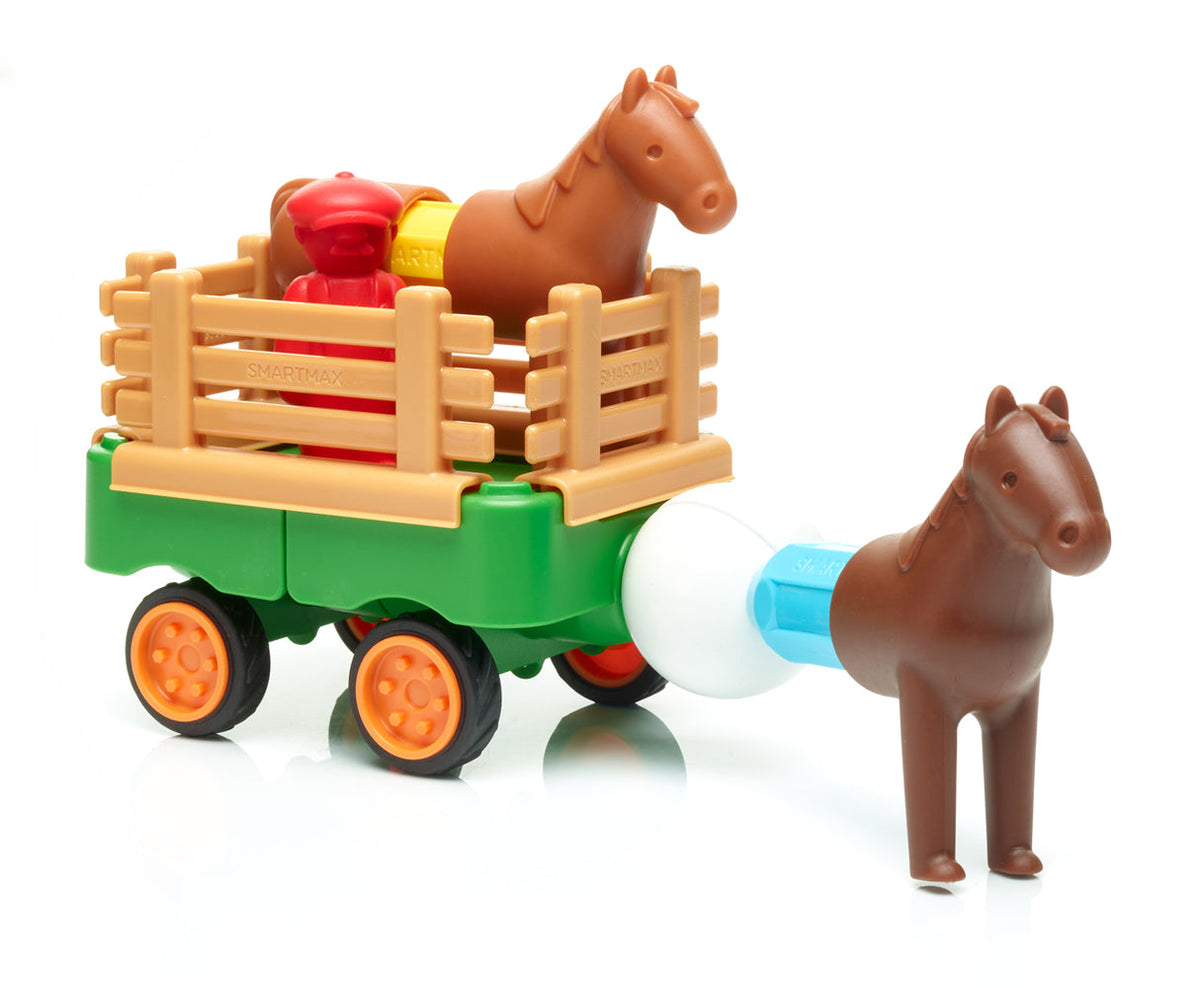 A green magnetic toy tractor with orange wheels hauling a trailer loaded with a brown toy horse, a red farmer figure, and wooden-look fencing pieces, while another brown toy horse is magnetically connected to the front.