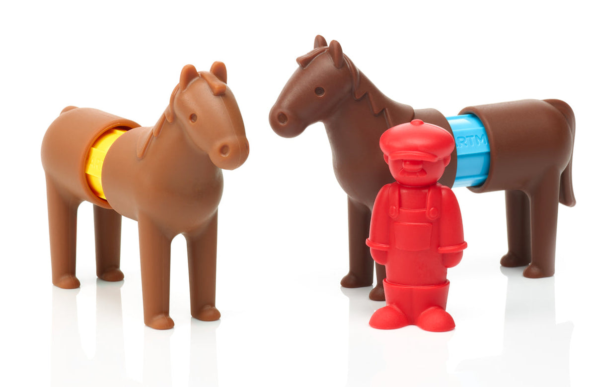 Two brown toy horses standing inside a wooden-look fenced enclosure, accompanied by a red farmer figure.