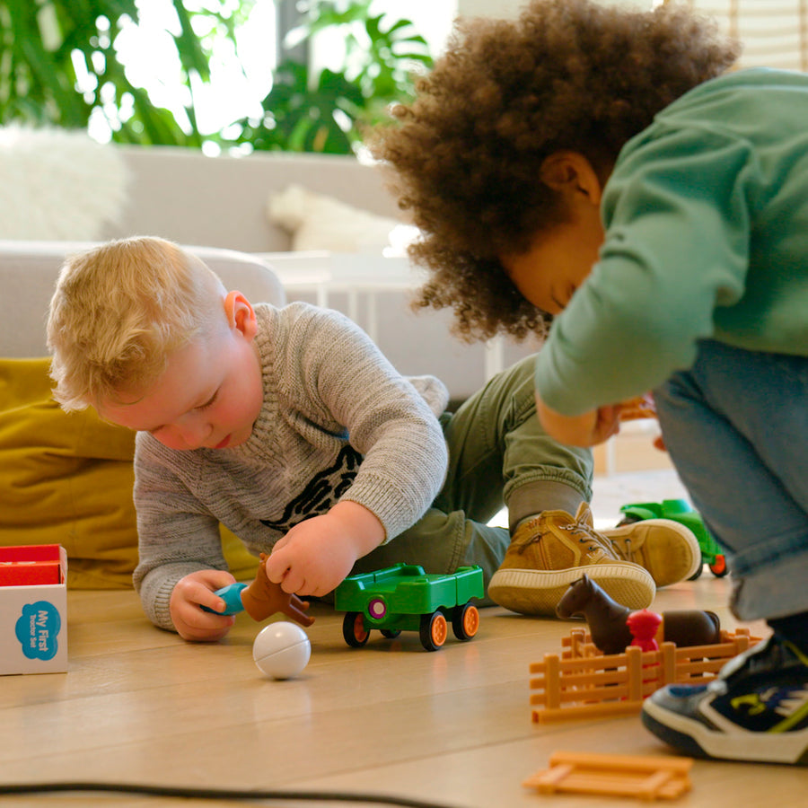 Two young children playing on the floor together with the green Smartmax My First Farm Tractor set, assembling the magnetic pieces near the open product box.