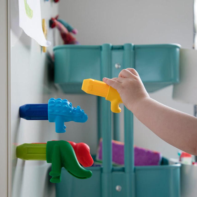Child's hand interacting with colorful magnetic toy dinosaurs on a refrigerator door.