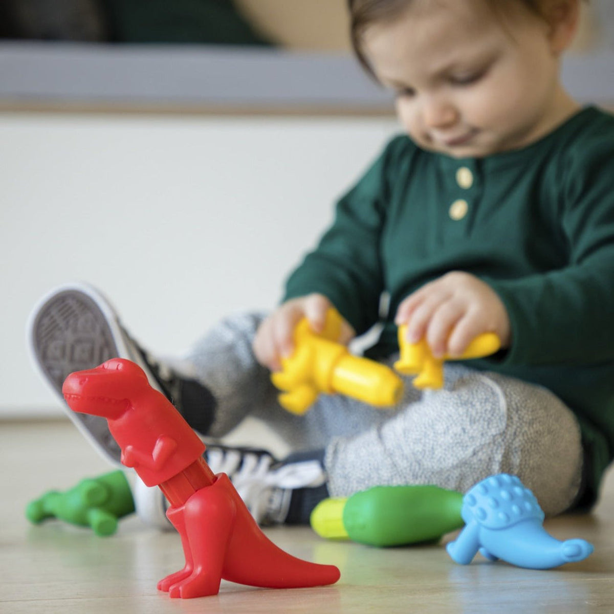 Child playing with colorful toy dinosaurs on a wooden floor.