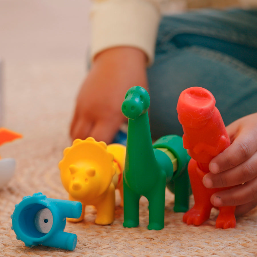 Colorful plastic animal toys on a carpeted floor with a child's hand holding a red toy.