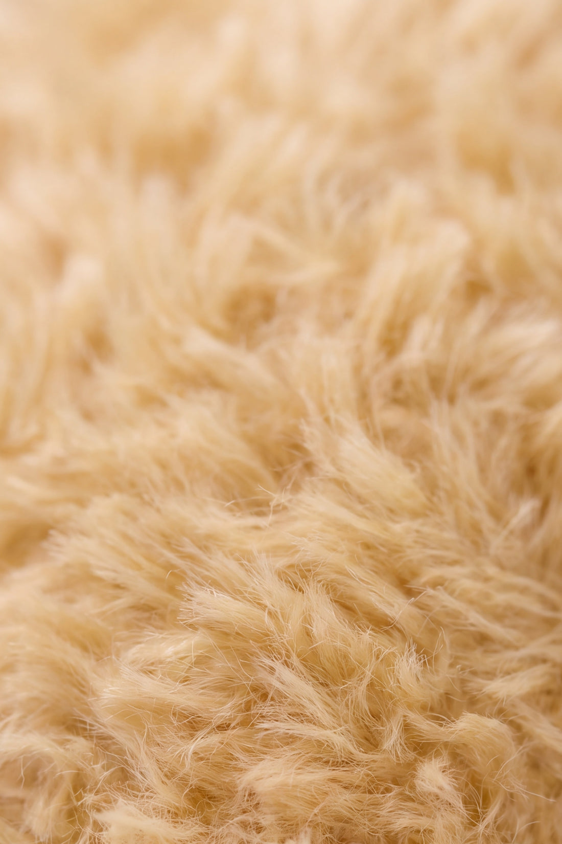 A close-up macro studio shot of the soft, honey-toned textured faux fur belonging to the "Snuggle Bunnies - Honey the Puppy by Jamie Kay" plush toy, highlighting the dense, fluffy pile and warm golden-brown color variations.