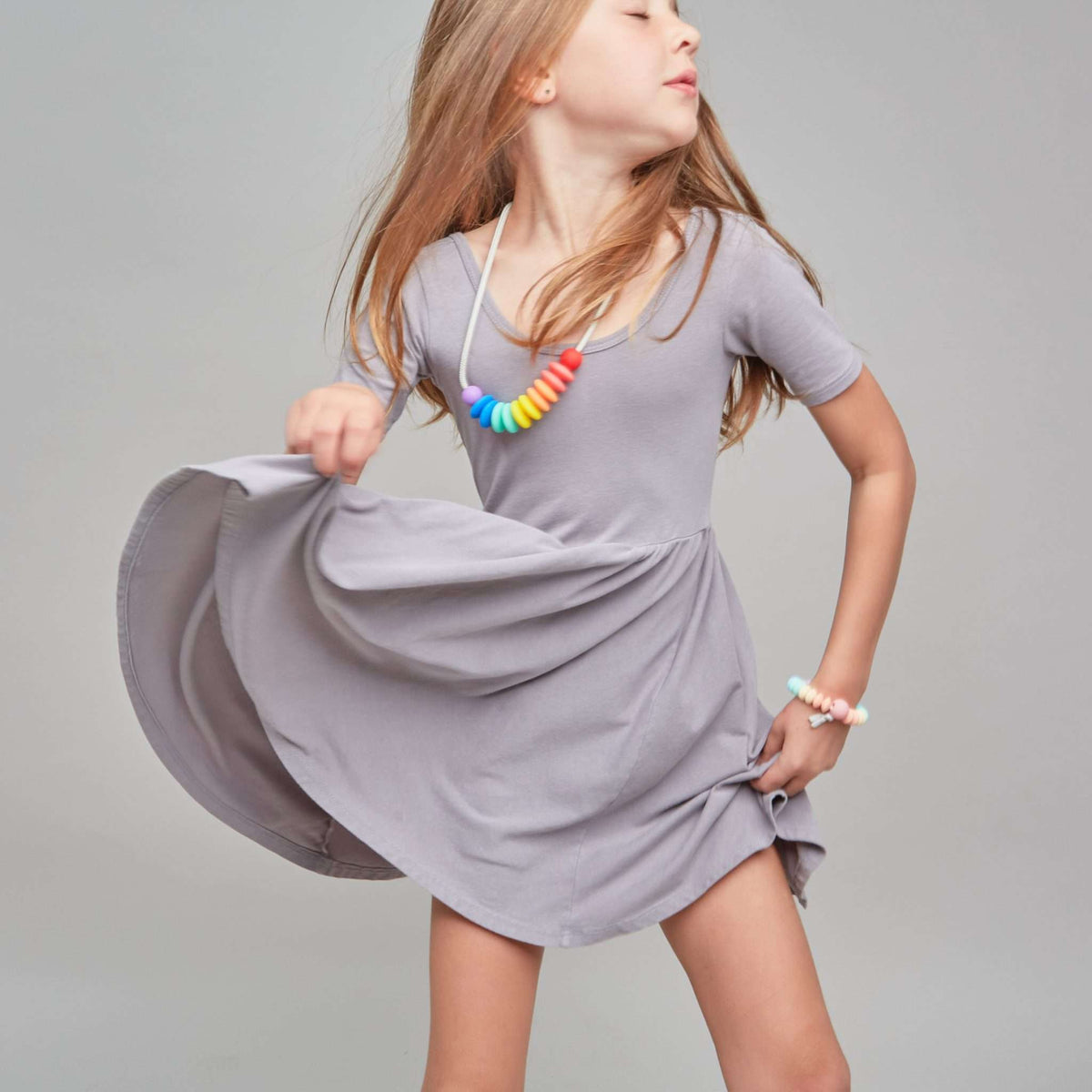 Young girl in a gray dress with a colorful necklace against a plain background