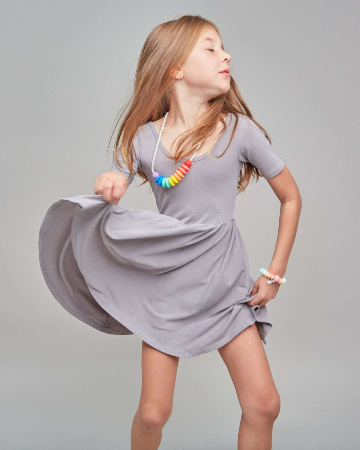 Young girl in a gray dress with a colorful necklace against a plain background
