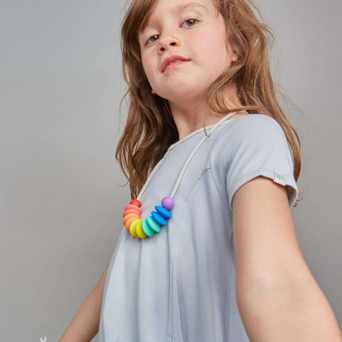 Young girl wearing a colorful necklace against a plain background